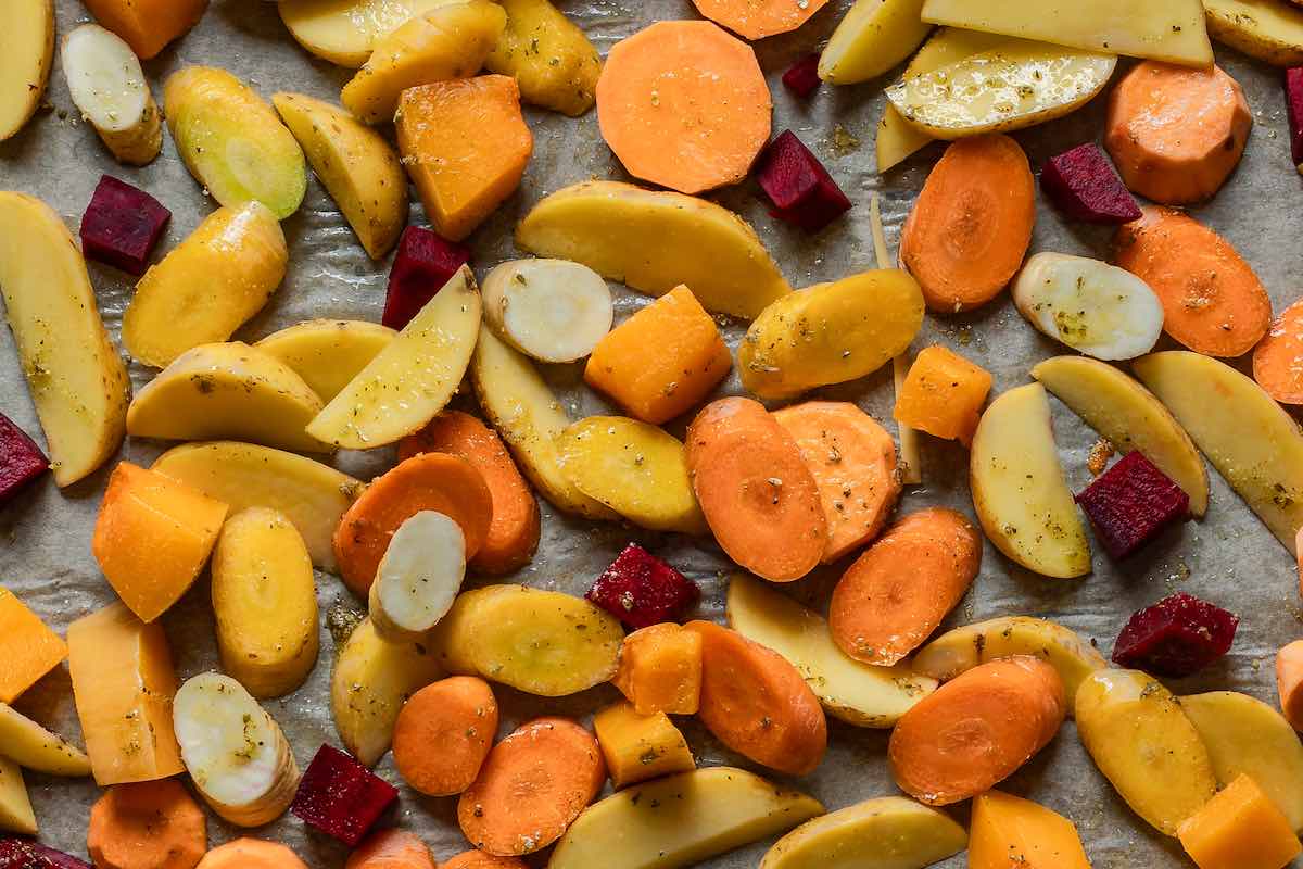 raw seasoned root vegetables on a lined baking sheet.