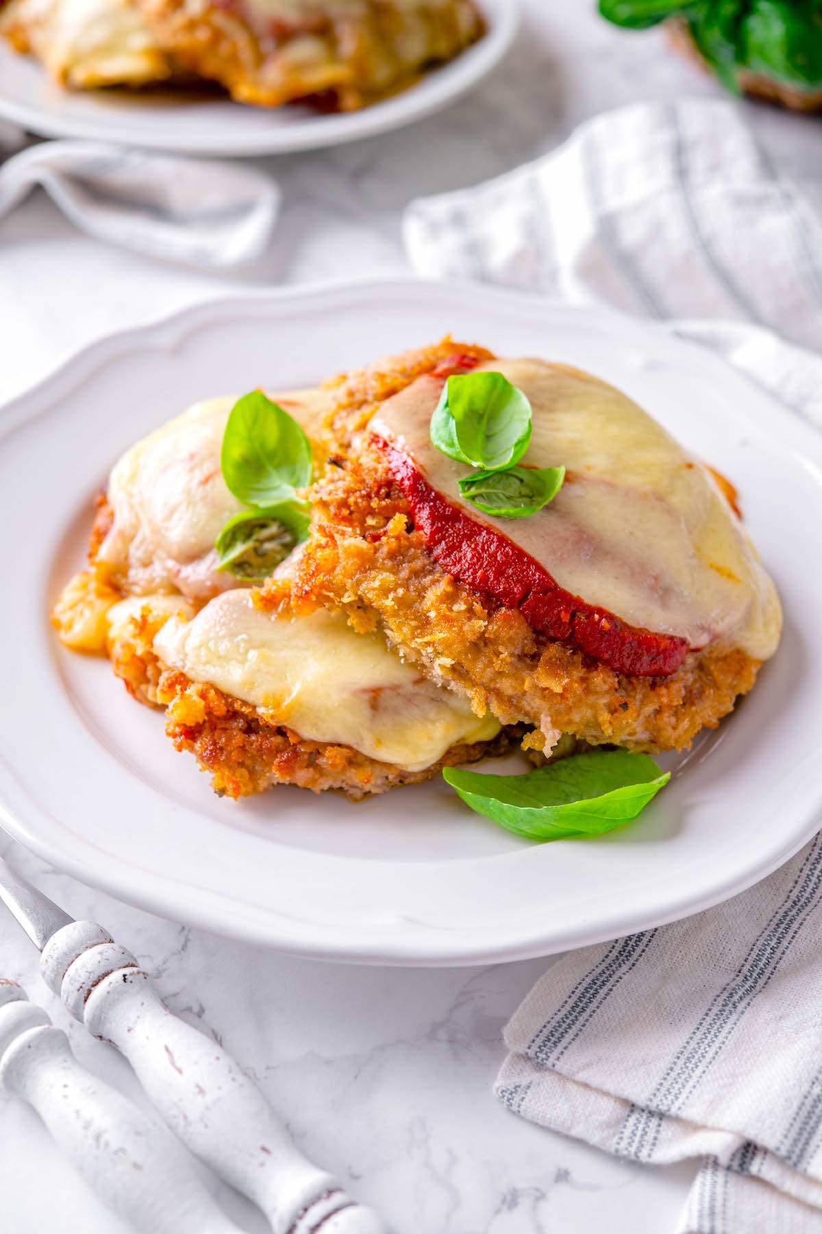 veal parmesan on a plate with fresh basil leaves.