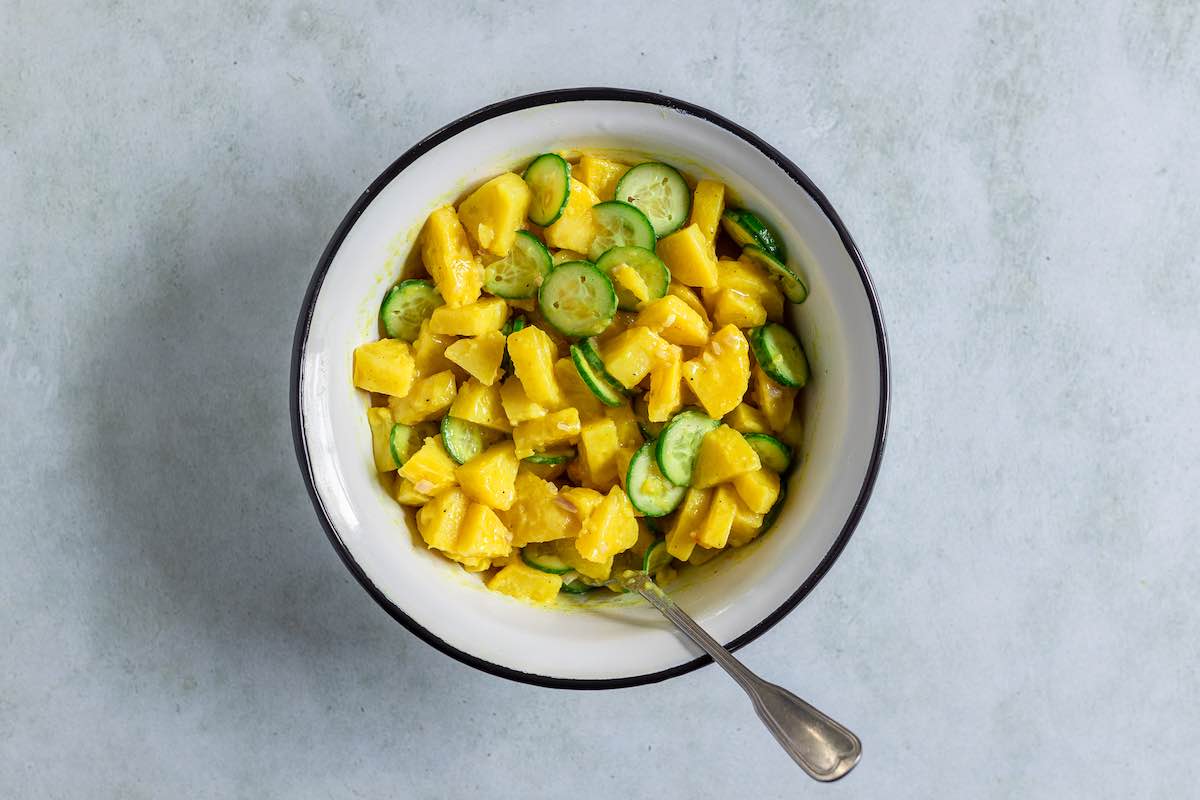 assembling potato salad in a bowl with cucumber.