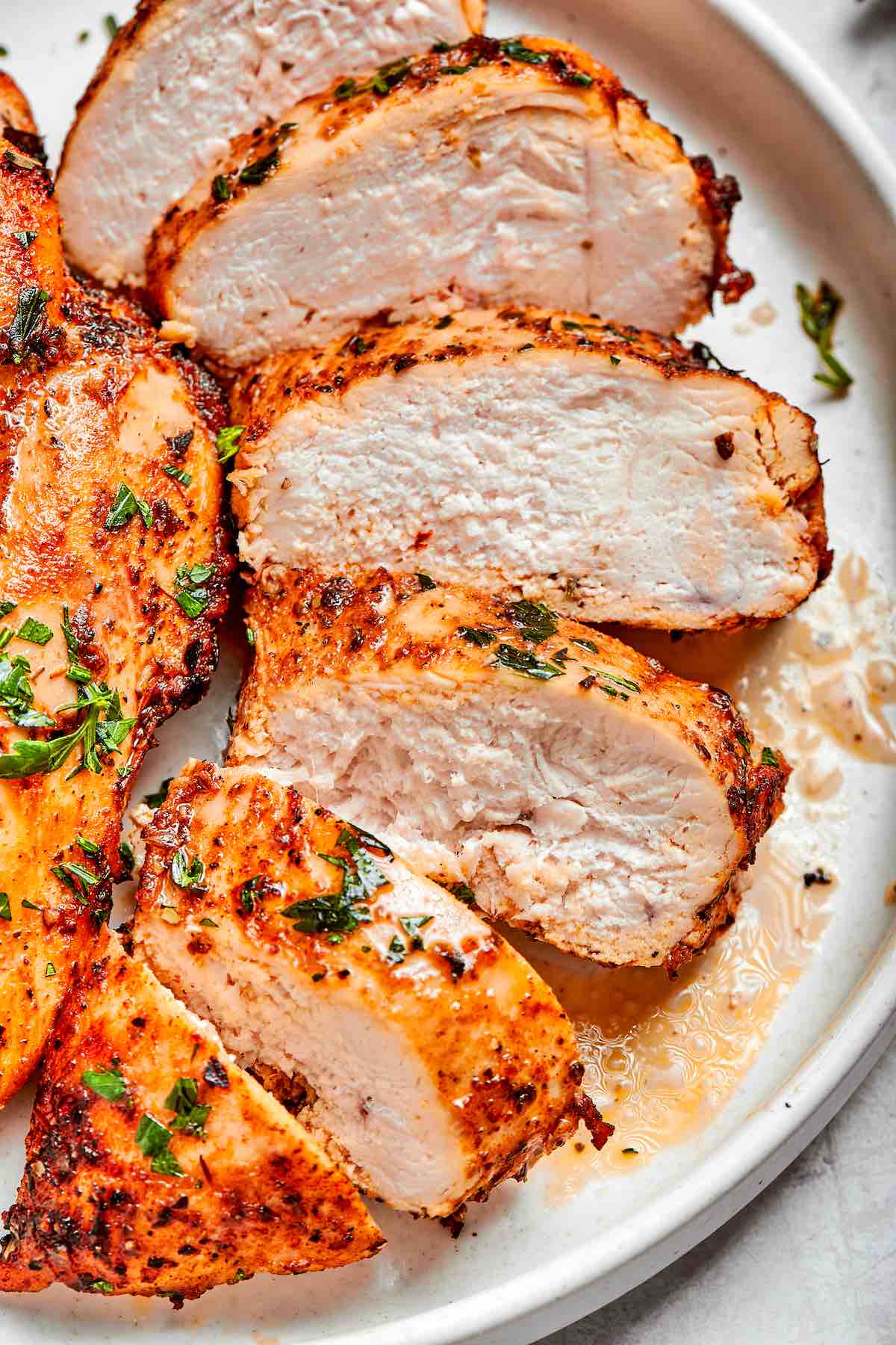 sliced air fried chicken breast on a white plate.
