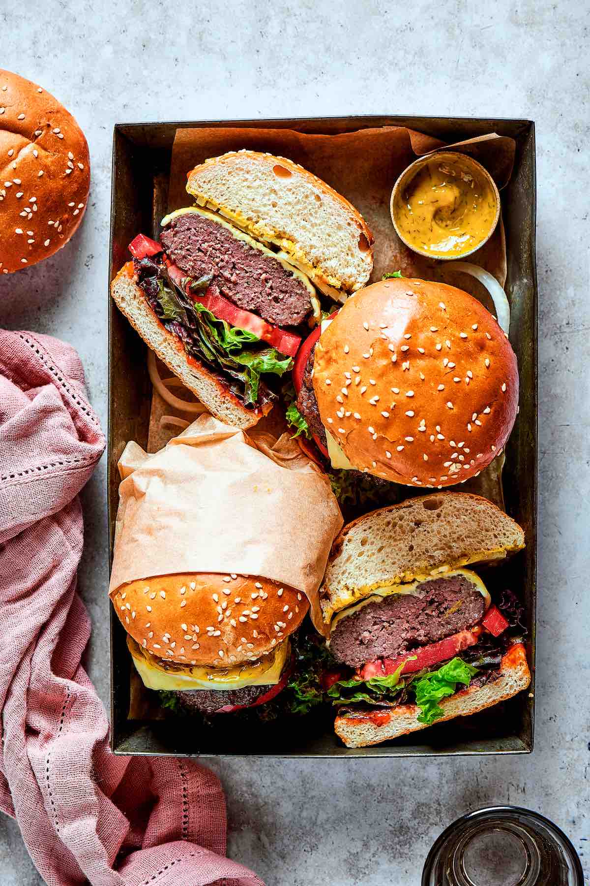 homemade bison burgers in a serving dish with mustard, cheese, and burger buns.