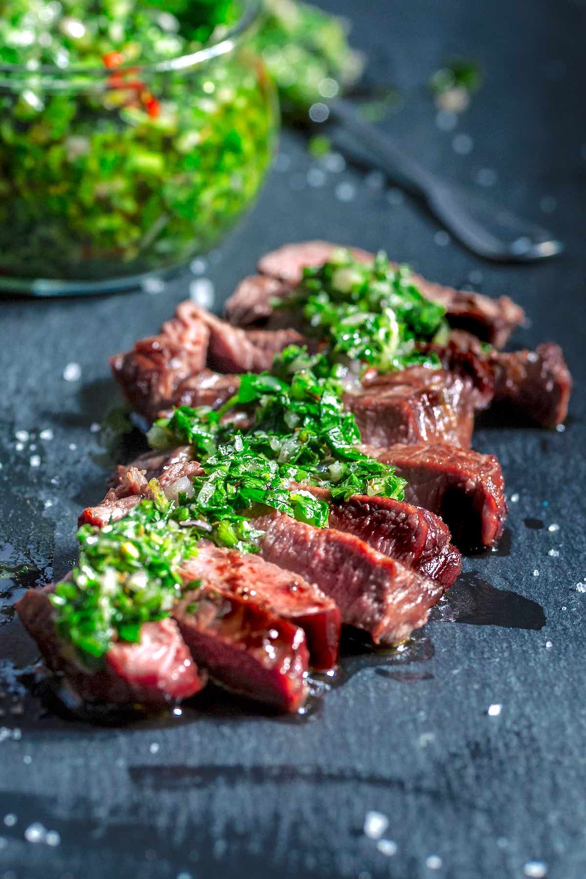 sliced steak with chimichurri sauce on top.