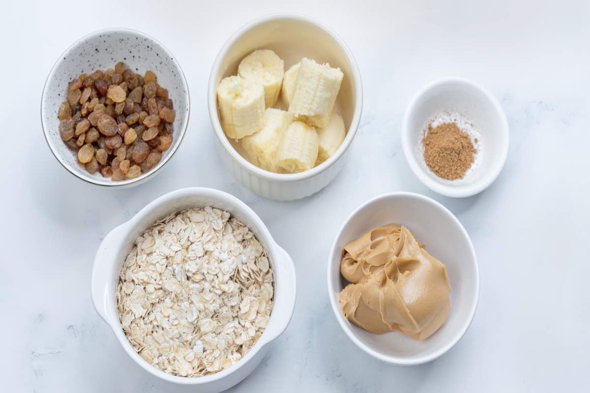 bowl of oats, bowl of almond butter, bowl of raisins, bowl of bananas, and small saucer with cinnamon.