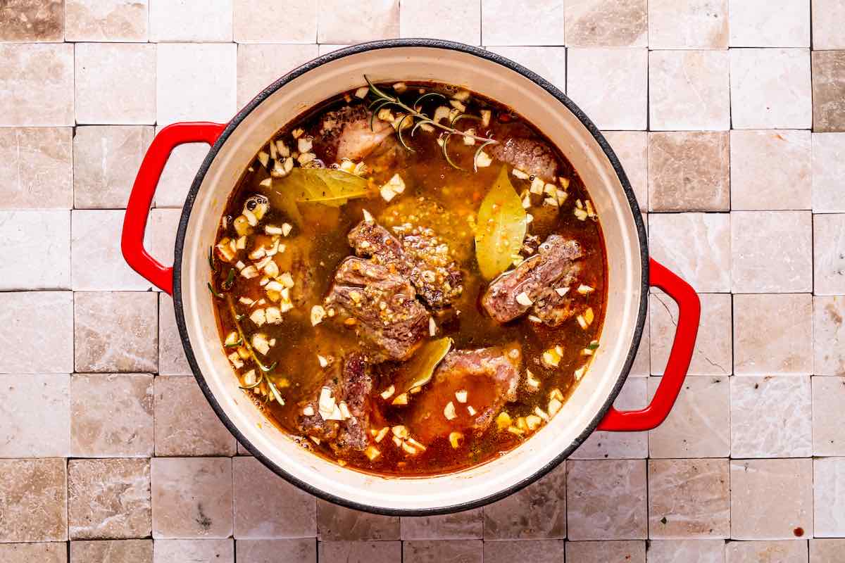 braising liquid added to Dutch oven with seared beef chuck short ribs.