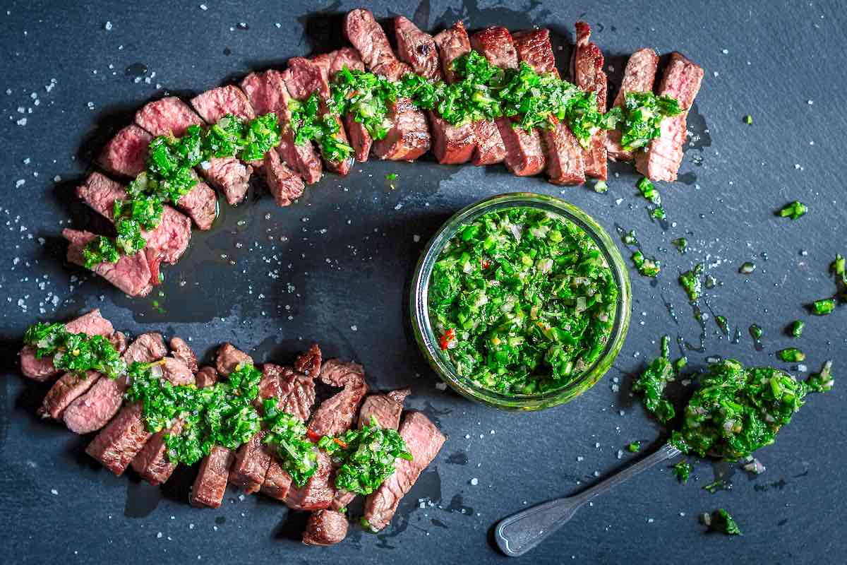 sliced steak with chimichurri sauce drizzled on top.