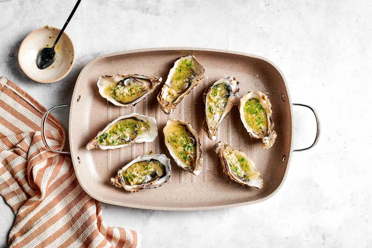 grilled oysters on a grill pan with garlic butter sauce drizzled on top.