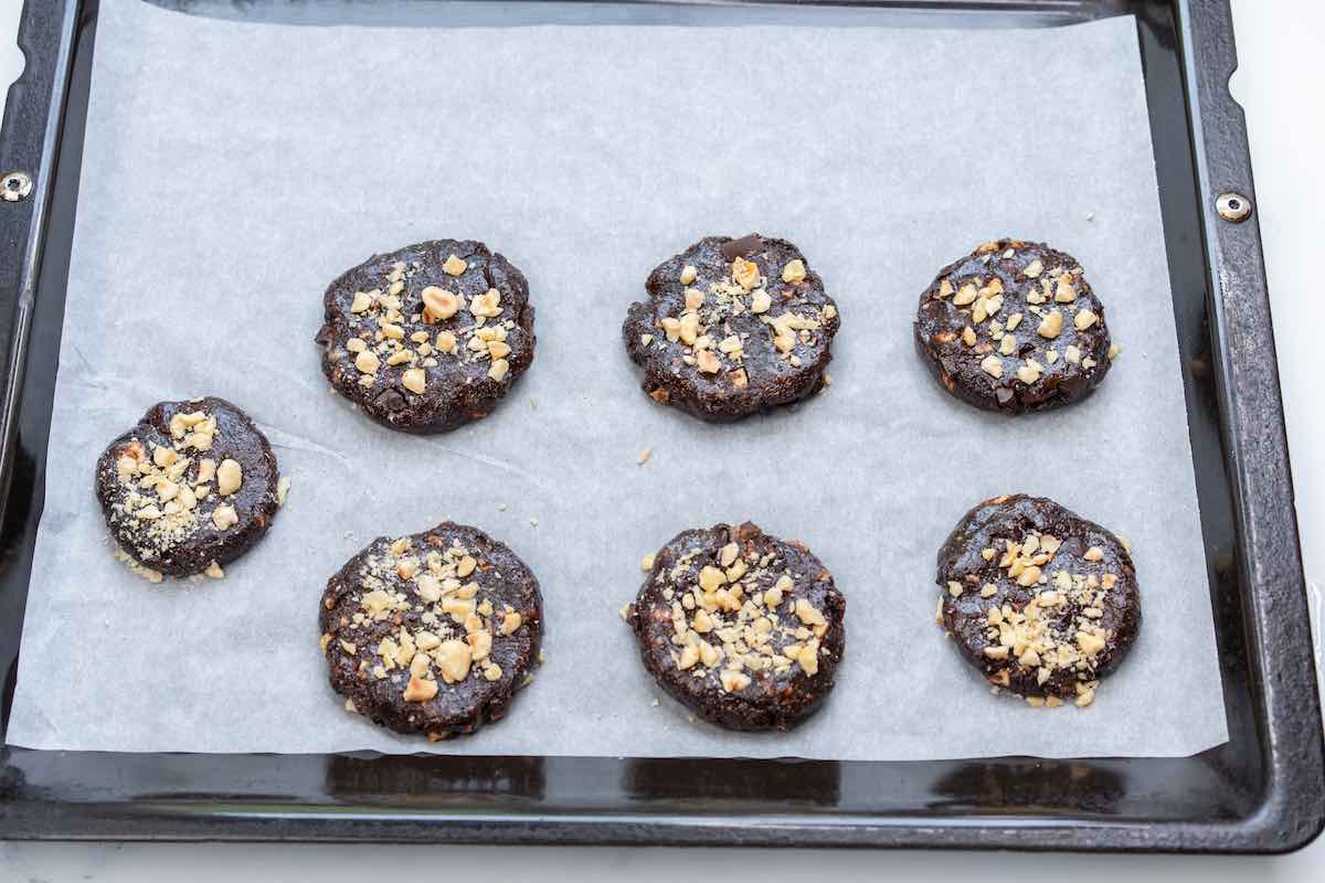 shaped unbaked cookies on a baking sheet with chopped hazelnuts on top.