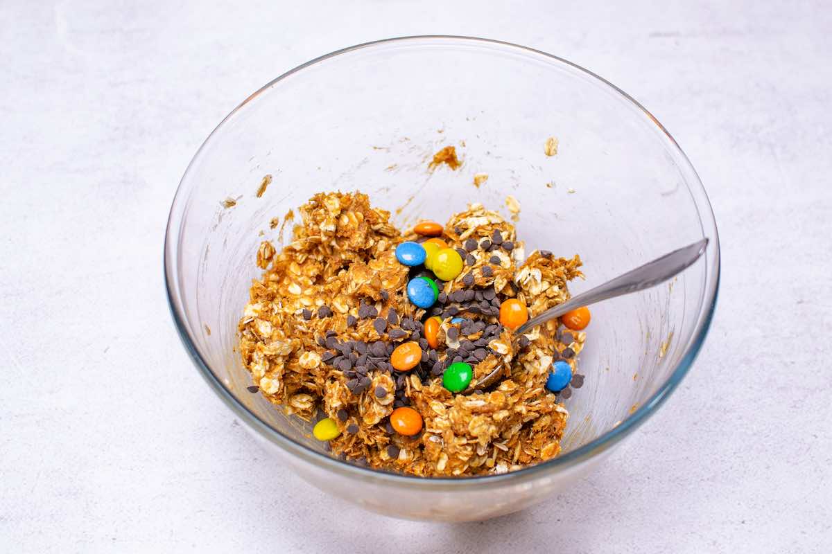 oats, peanut butter, banana, chocolate chips, and m&m's in a bowl.