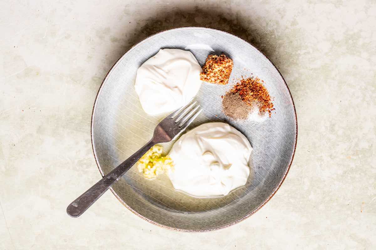 Greek yogurt, mayonnaise, Dijon mustard, and seasonings on a plate.v