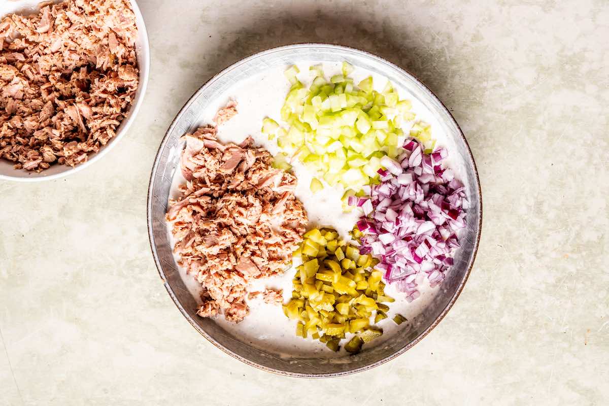 flaked tuna, chopped pickles, chopped celery, and chopped red onion on a plate.