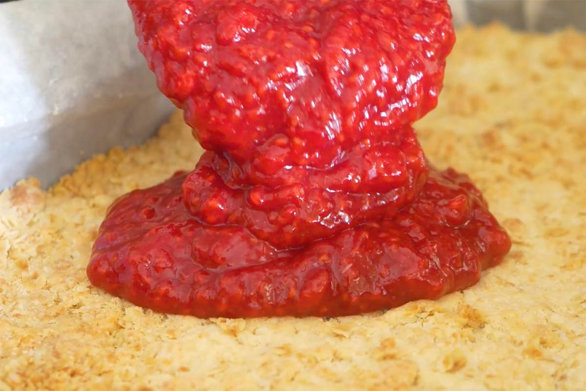 pouring raspberry jam over the crust.