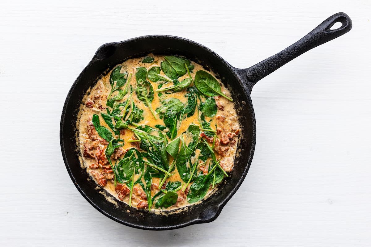 creamy Tuscan sauce with spinach and sun dried tomatoes in a skillet. 