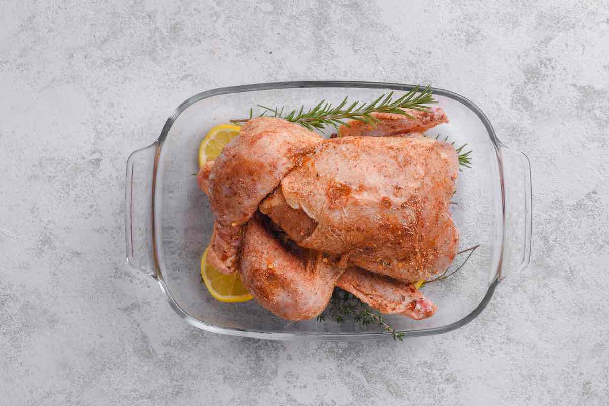 seasoned raw cornish hen in a baking dish over sliced lemon and herbs.