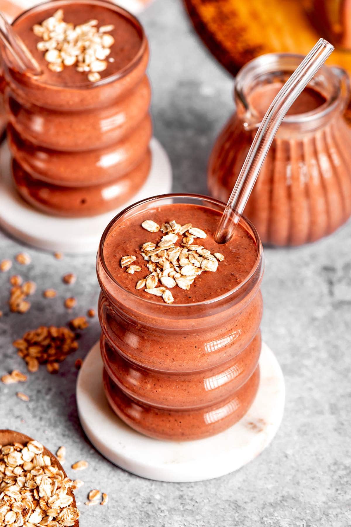 brownie batter oatmeal smoothie in a glass with rolled oats on top.