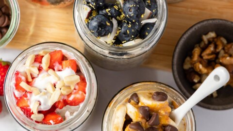 overhead shot of overnight oats with protein powder in jars topped with white chocolate and raspberries, peanut butter, banana, and chocolate chips.