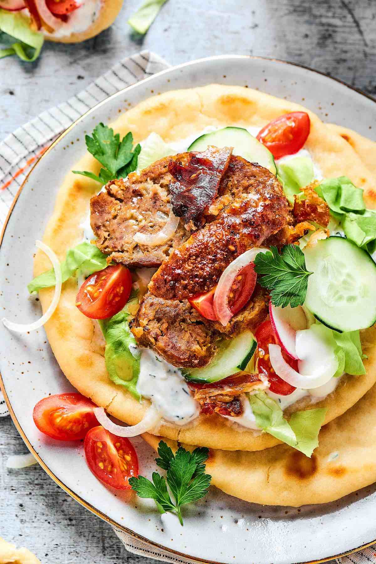 gyro meat on pita with garlic sauce, lettuce, tomato, and cucumber.