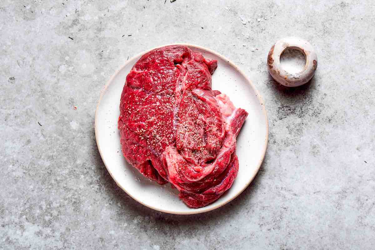 raw chuck roast seasoned with salt and pepper.