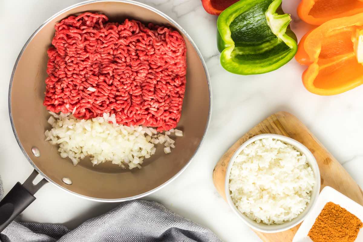 raw ground beef and diced onions cooking in a skillet.