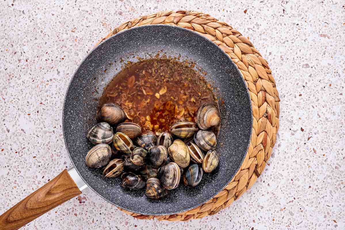 clam sauce simmering in a skillet with fresh clams.