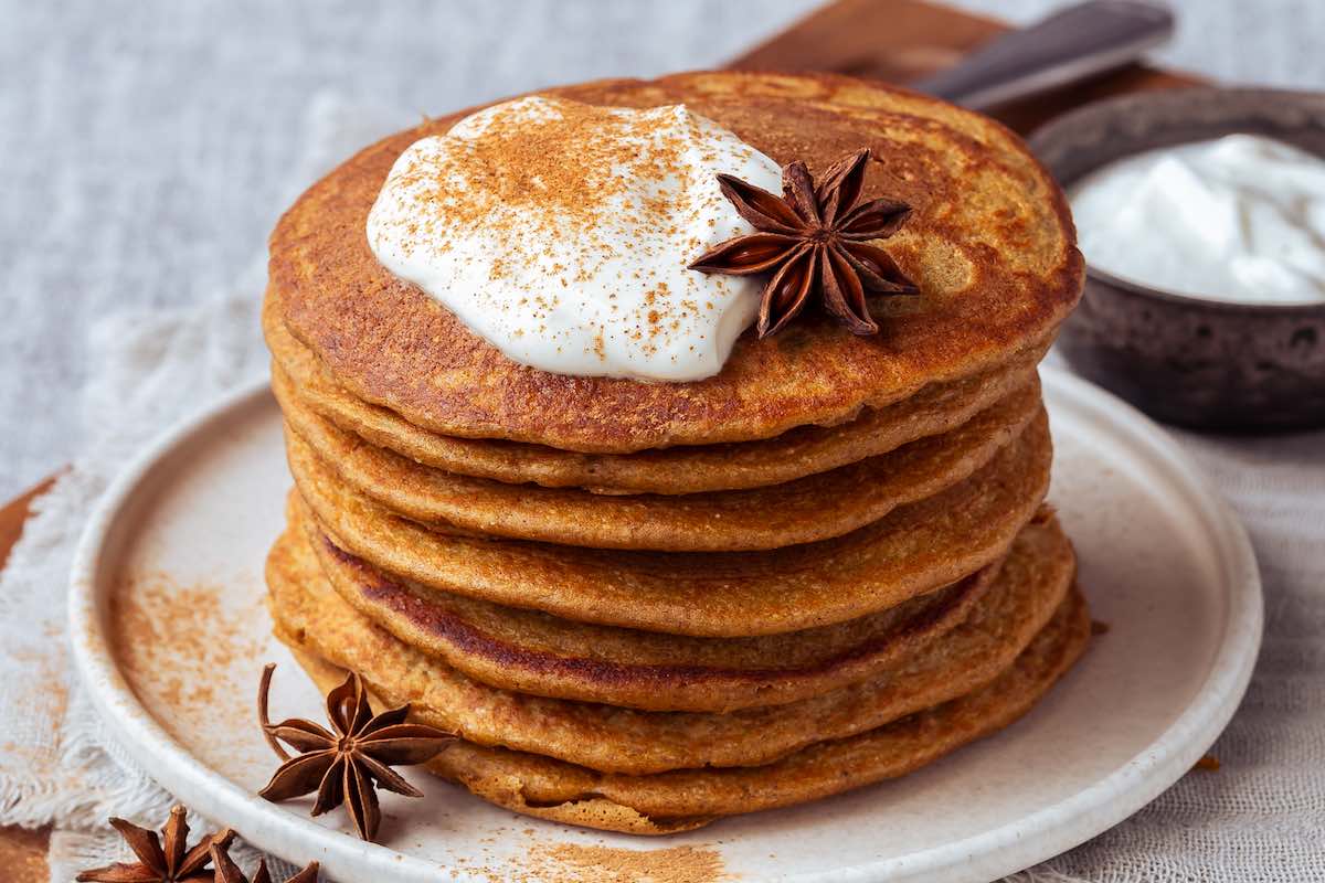 stack of pumpkin protein pancakes on a plate with Greek yogurt and cinnamon on top.