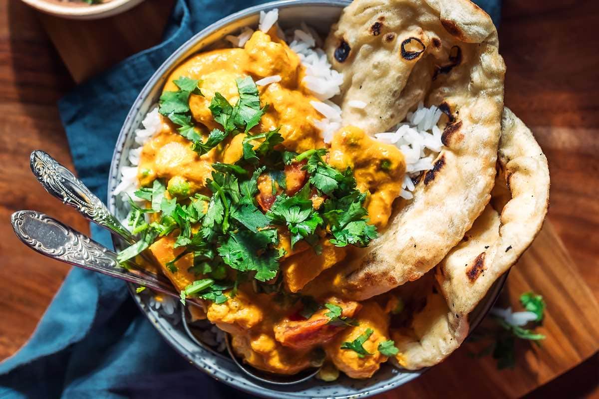 bowl of veggie korma with naan and chopped cilantro.