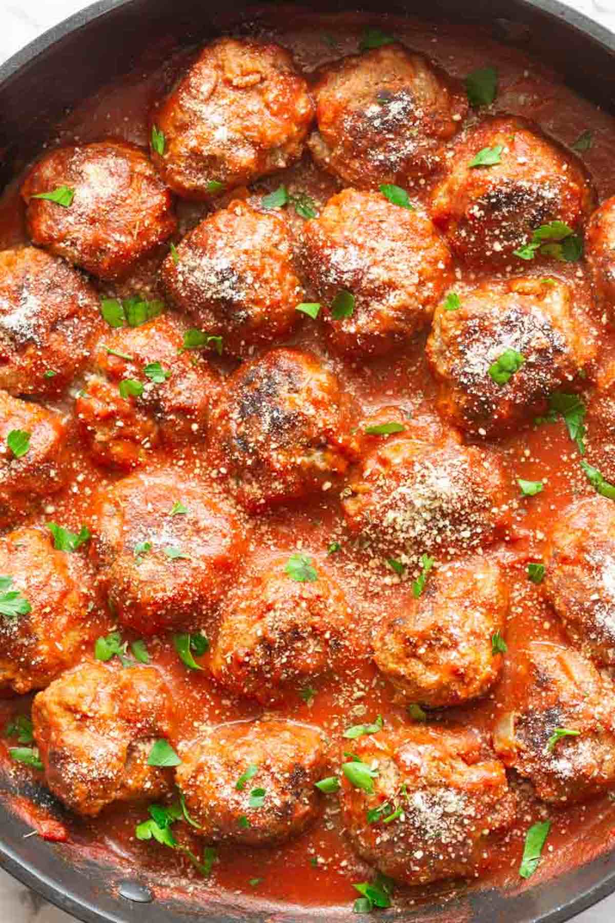 keto meatballs in a skillet with parmesan cheese and fresh herbs on top.