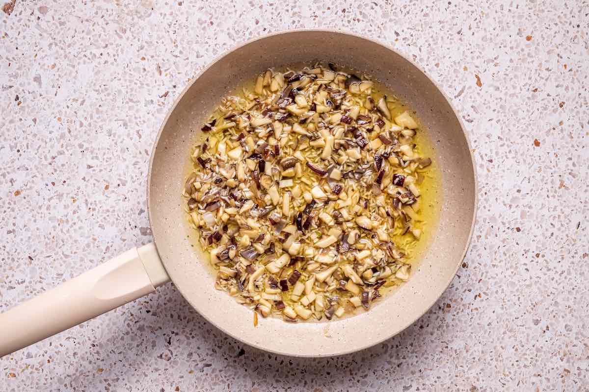 onions and oyster mushrooms sauteing in a skillet.