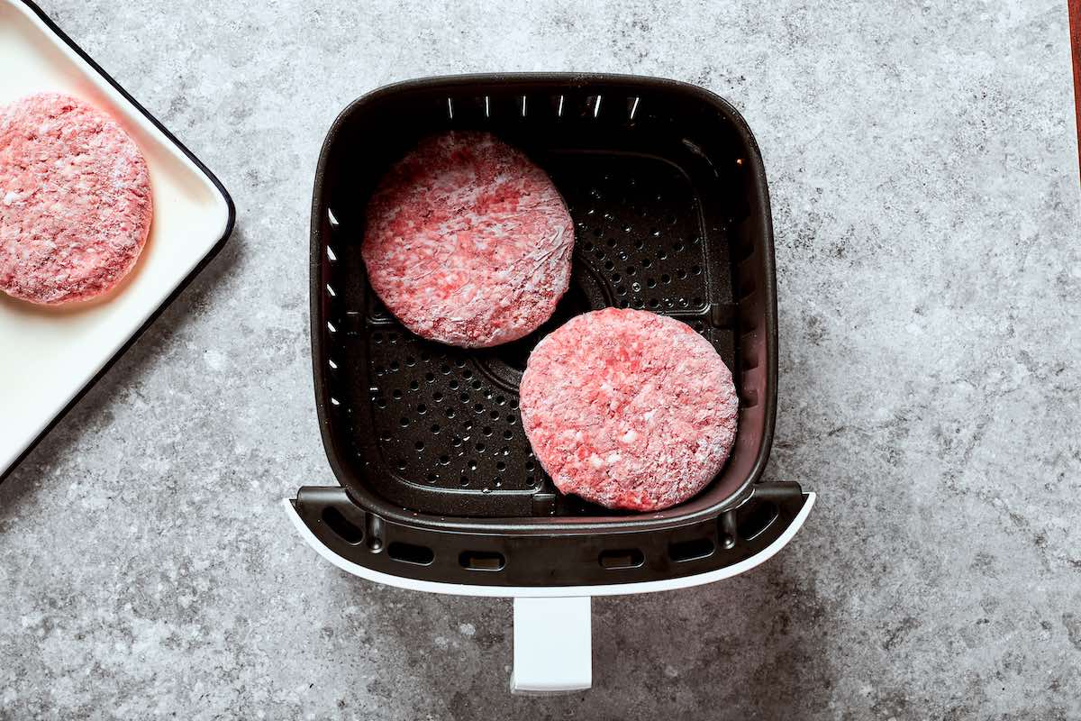 frozen hamburger patties in the air fryer basket.