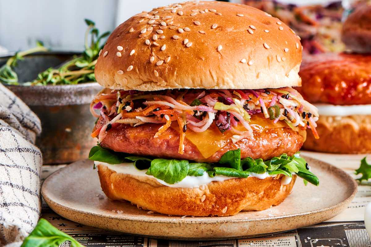 assembled burgers with slaw, cheese, salad, mayo, in a burger bun.