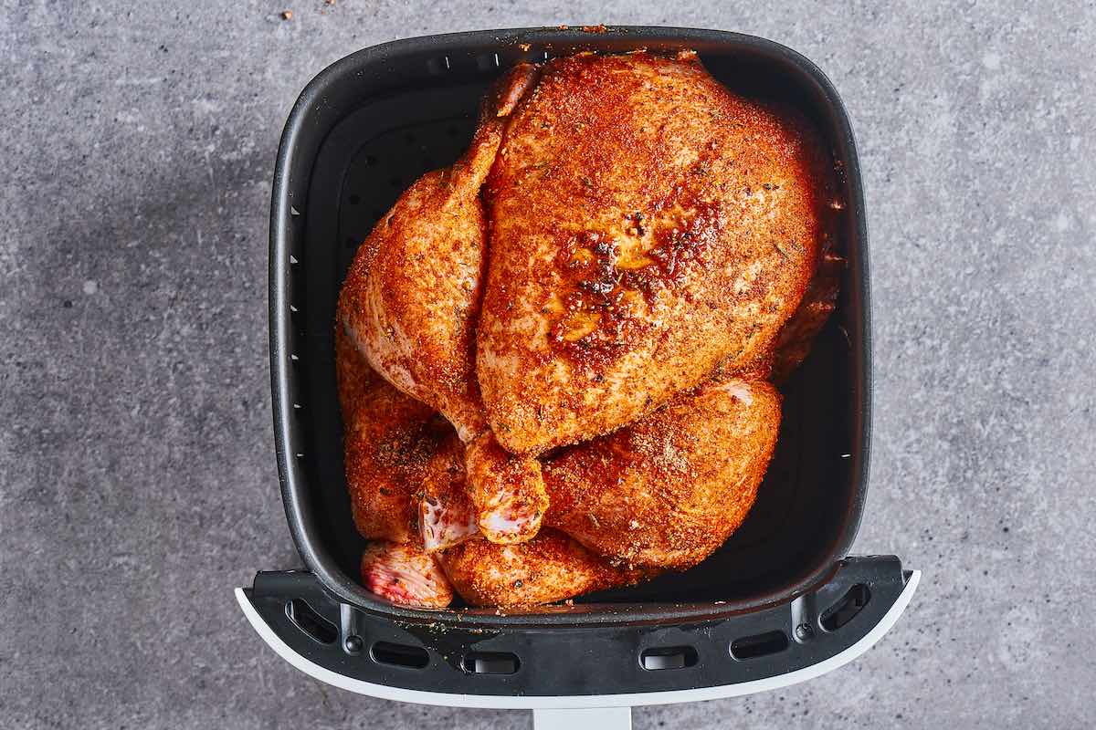 seasoned raw chicken in air fryer basket.