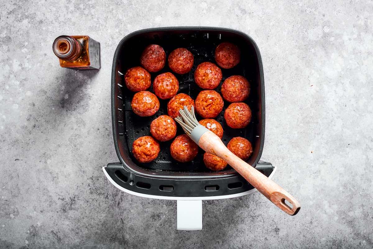brushing sauce on frozen meatballs.