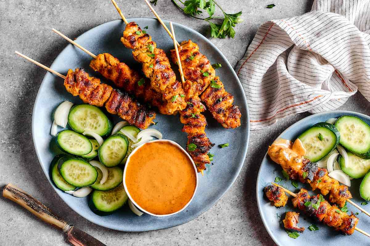 meat skewers served with peanut sauce and sliced cucumber.