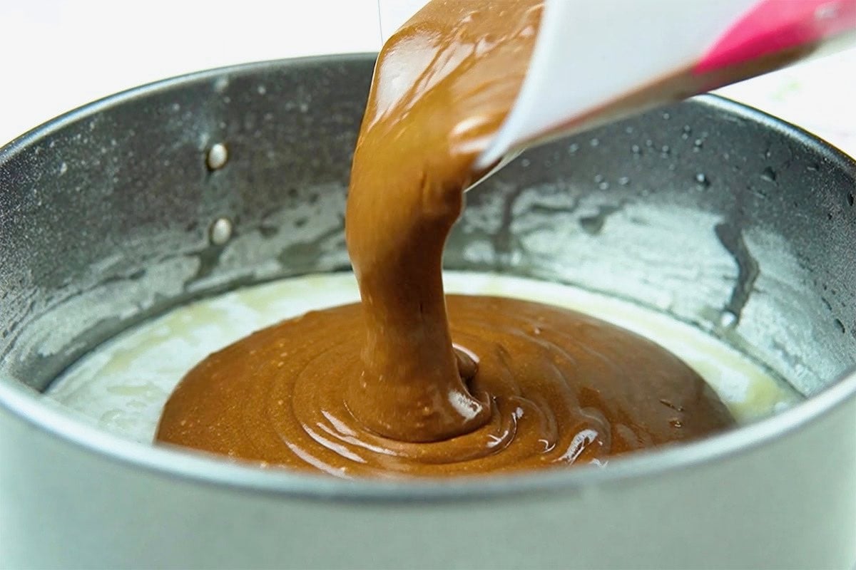 pouring vegan cake batter into cake pan.