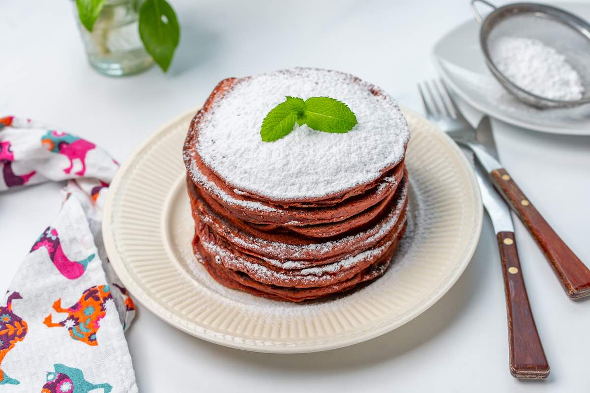 stack of red velvet pancakes with powdered sugar on top.
