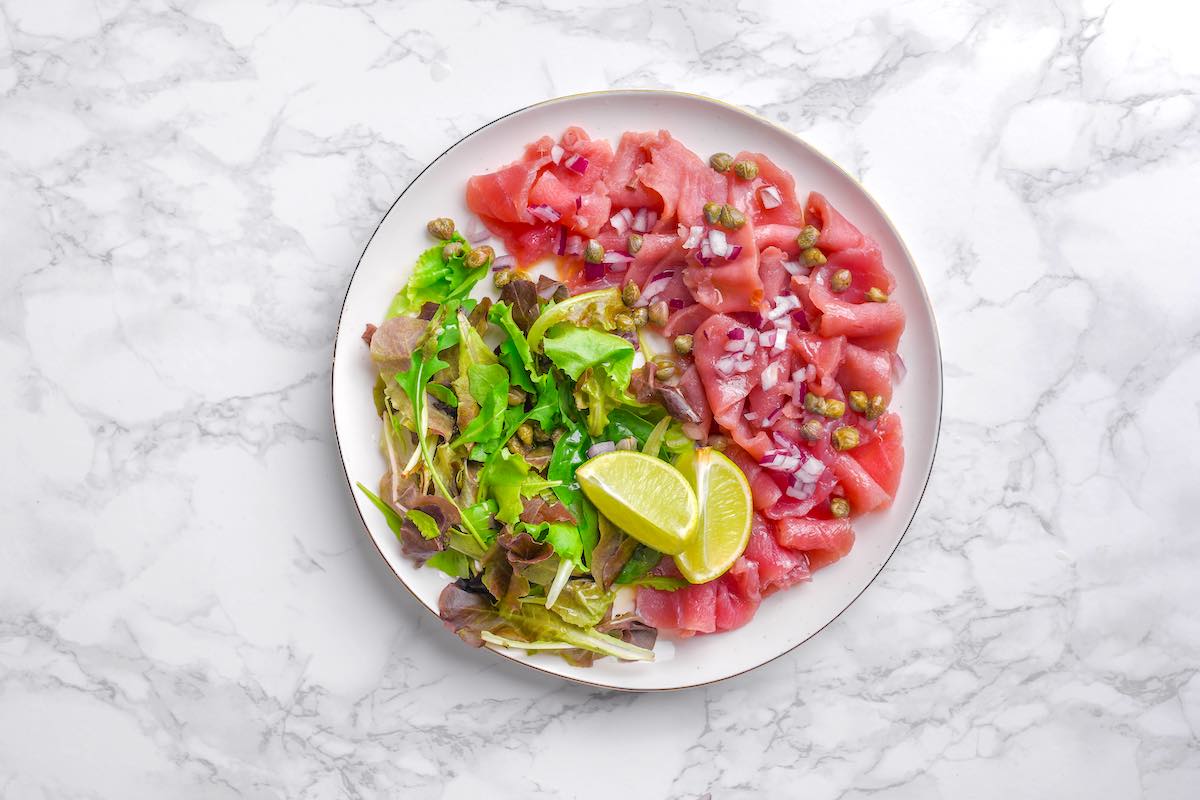 plate of tuna carpaccio with arugula and fresh lime.