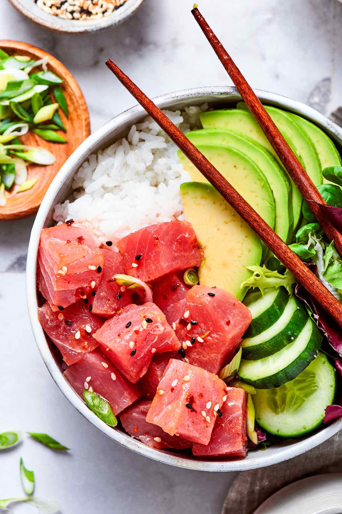 tuna poke bowl with sliced avocado, cucumber, mixed greens, and poke sauce.