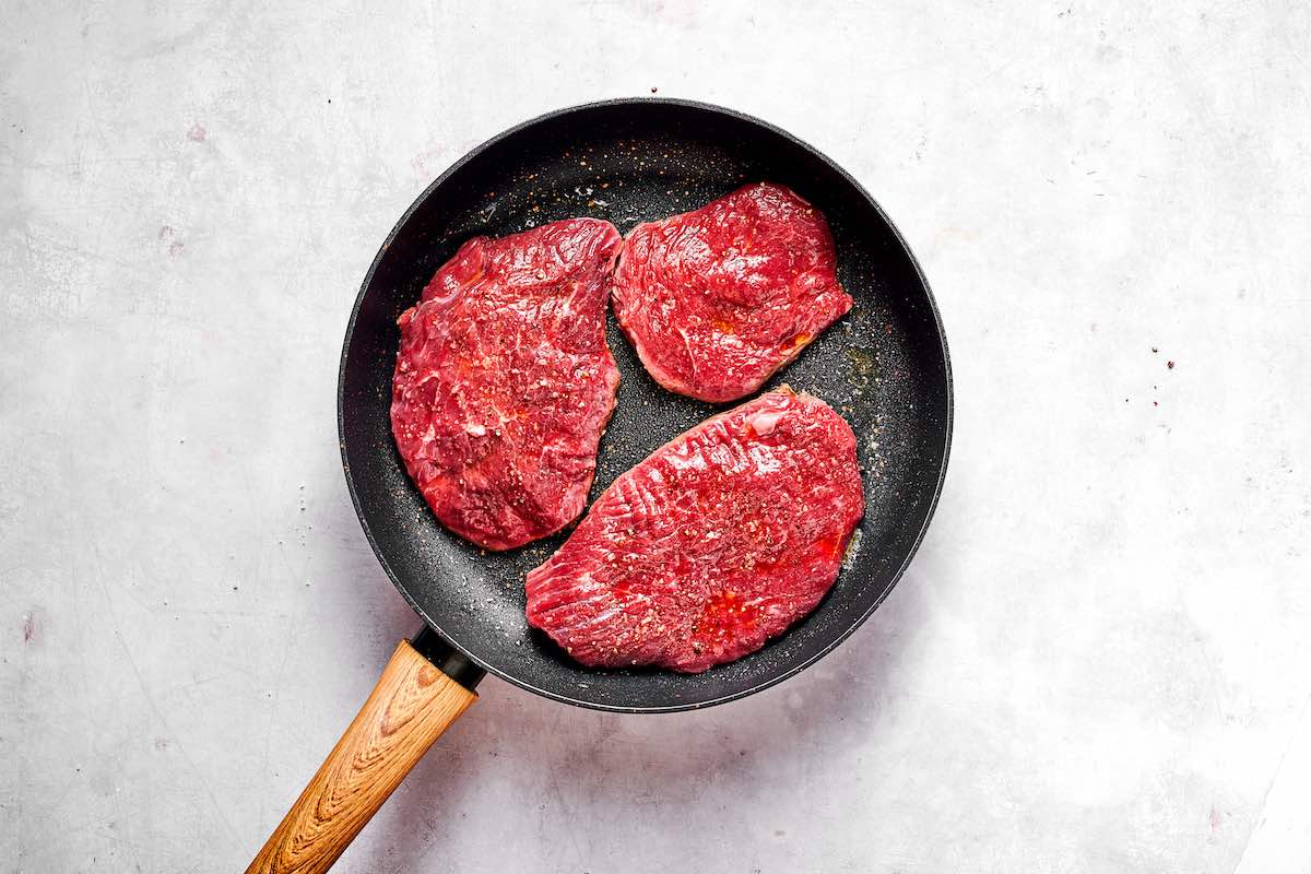 raw seasoned minute steaks in a skillet.