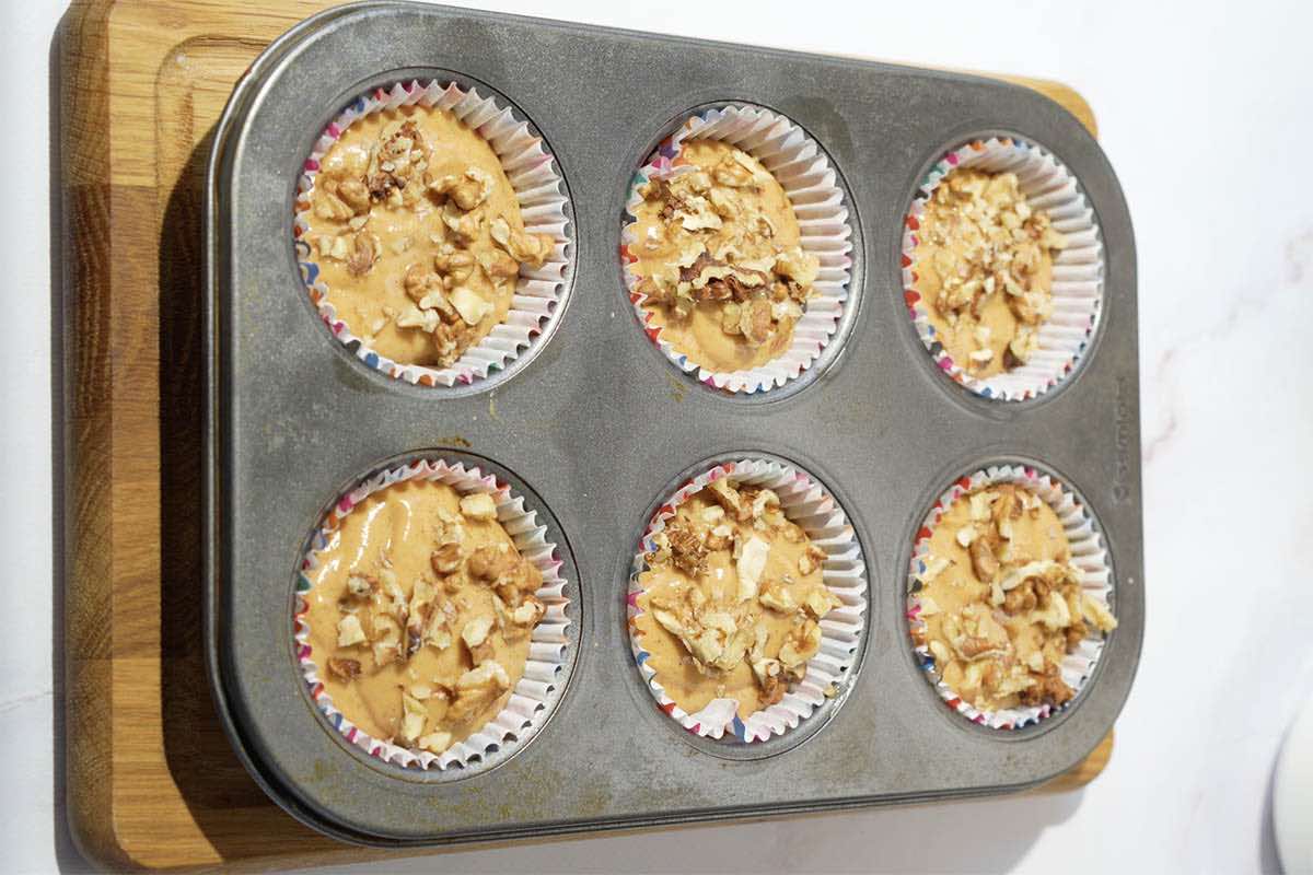 muffin batter in muffin liners with walnuts on top.