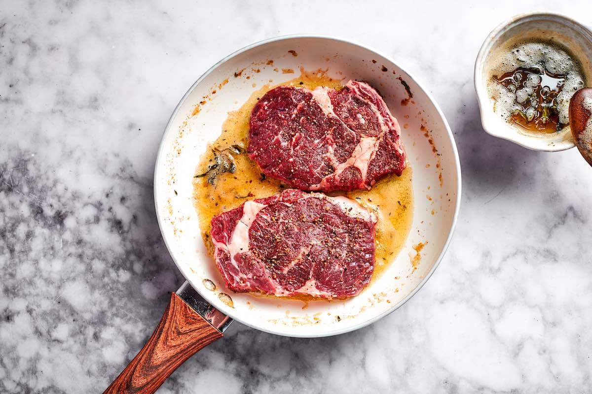 pan-searing ribeye steaks in a skillet.
