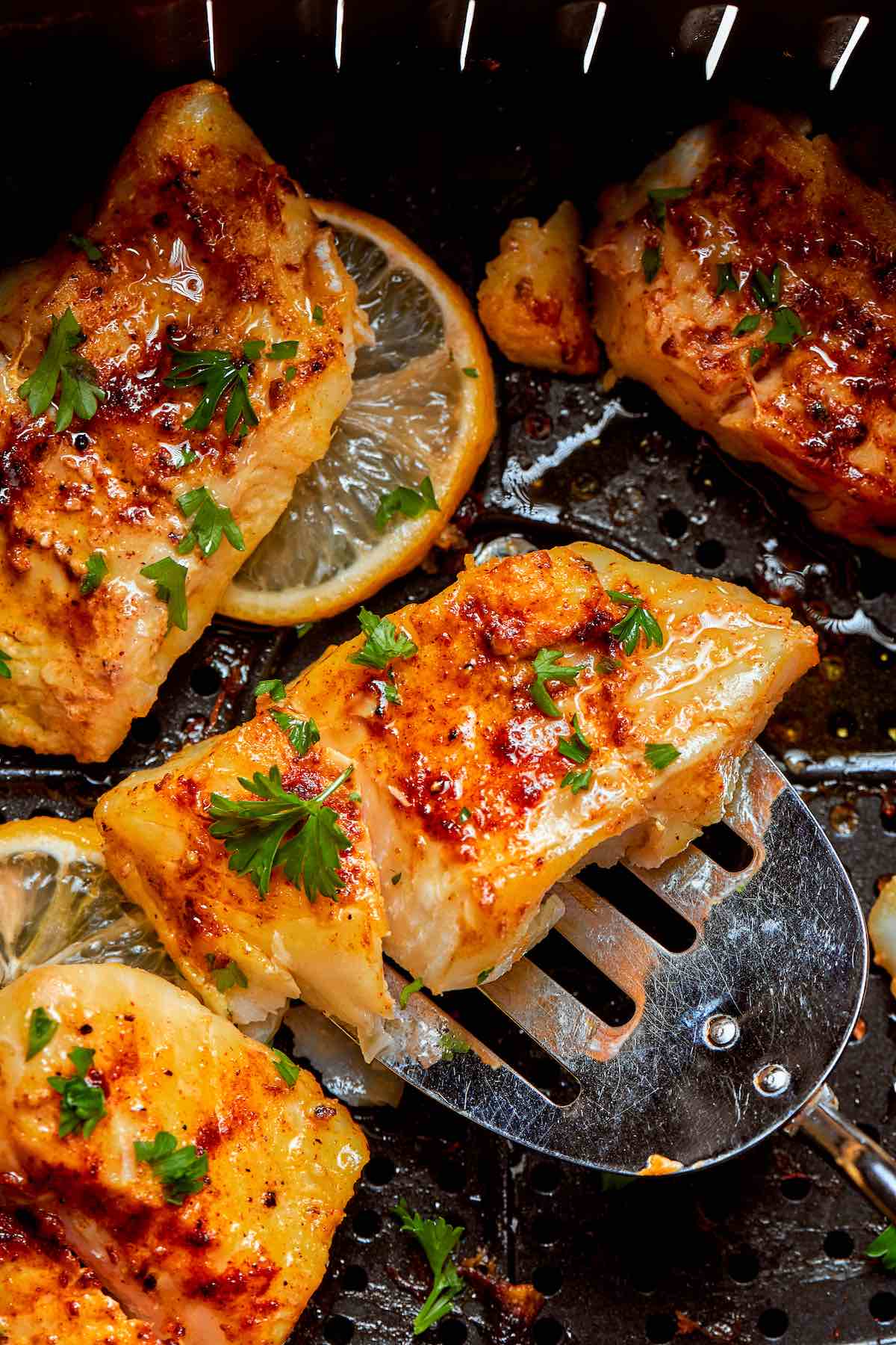 air fried halibut fillets in the air fryer with fresh lemon slices and chopped parsley.