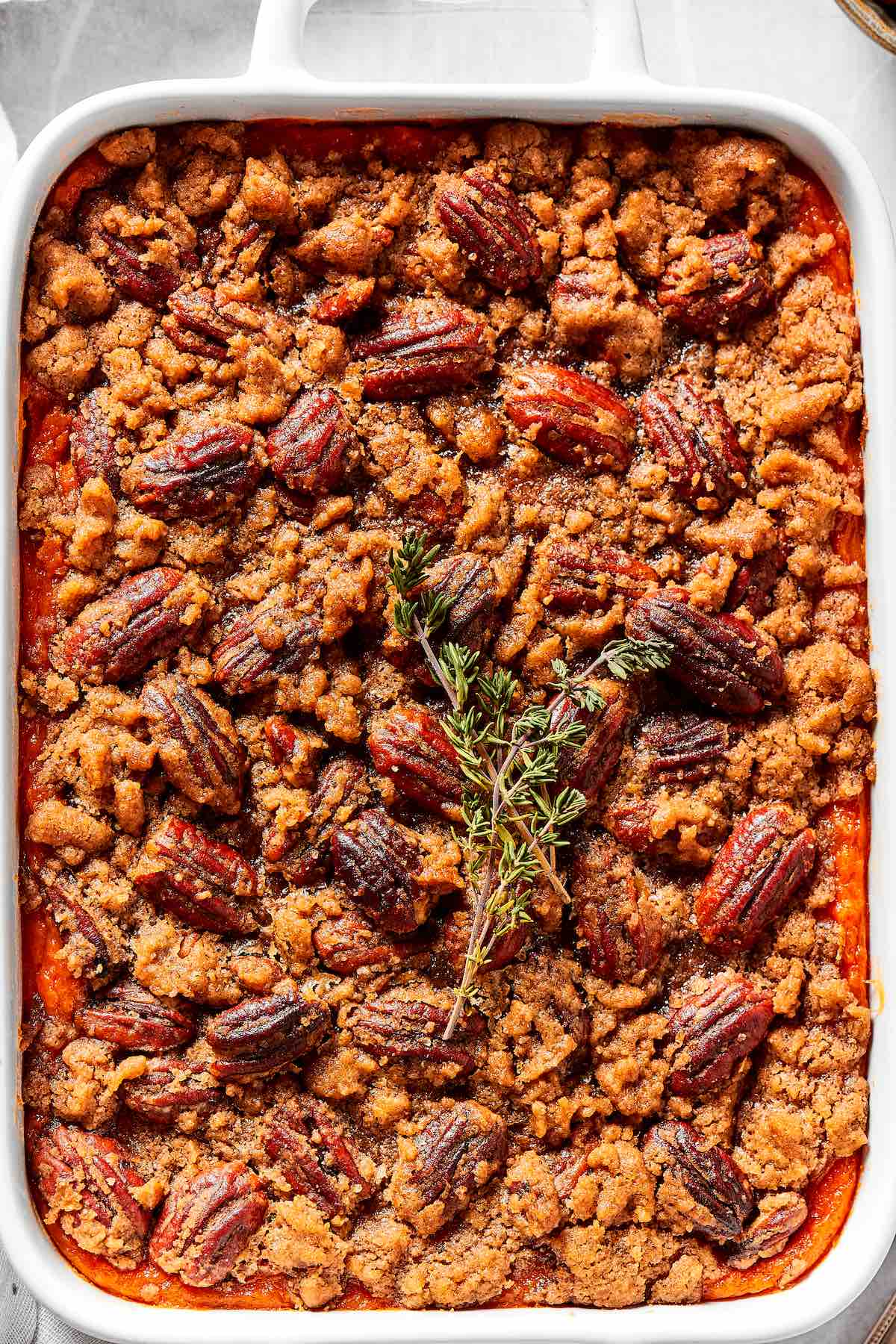 healthy sweet potato casserole in a baking dish with fresh rosemary on top.