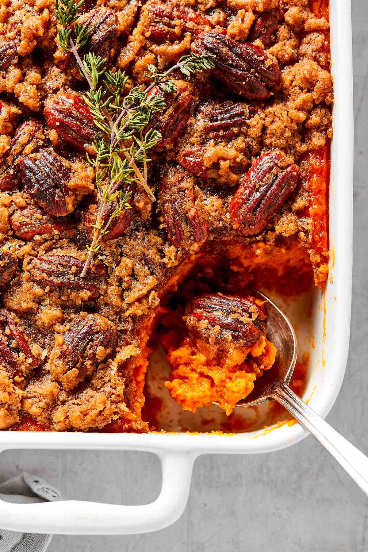 healthy sweet potato casserole in a white baking dish with a spoon coming out.