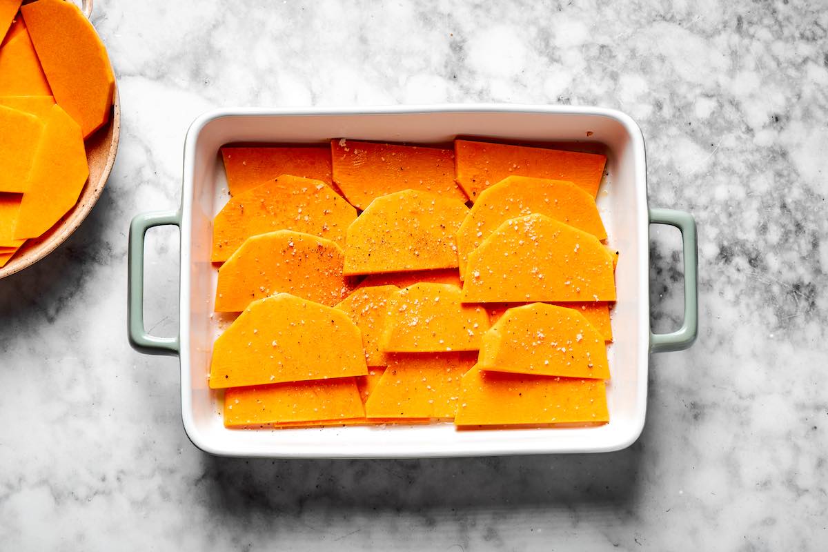 sliced and seasoned butternut squash layered in a baking dish.