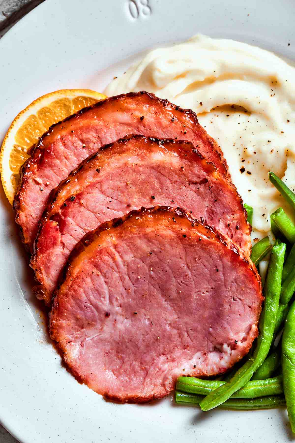 sliced air fryer ham over mashed potatoes with green beans.