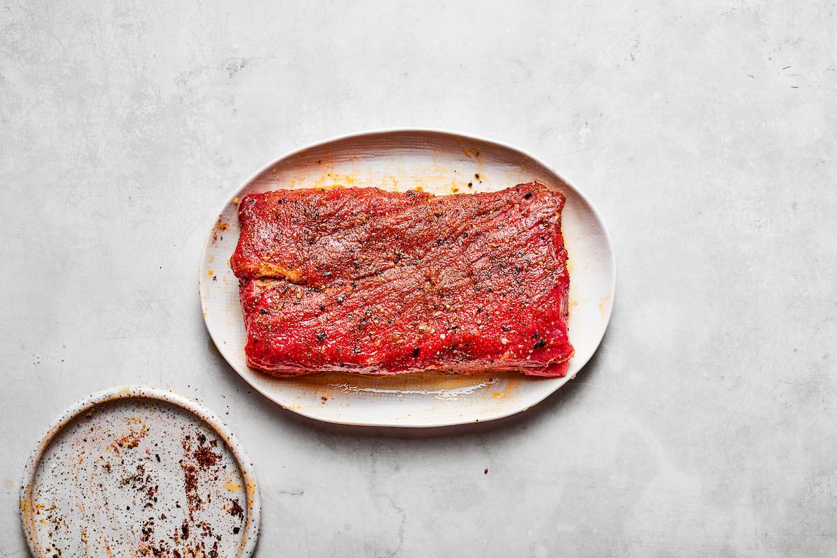 seasoned and raw tri tip on a plate.