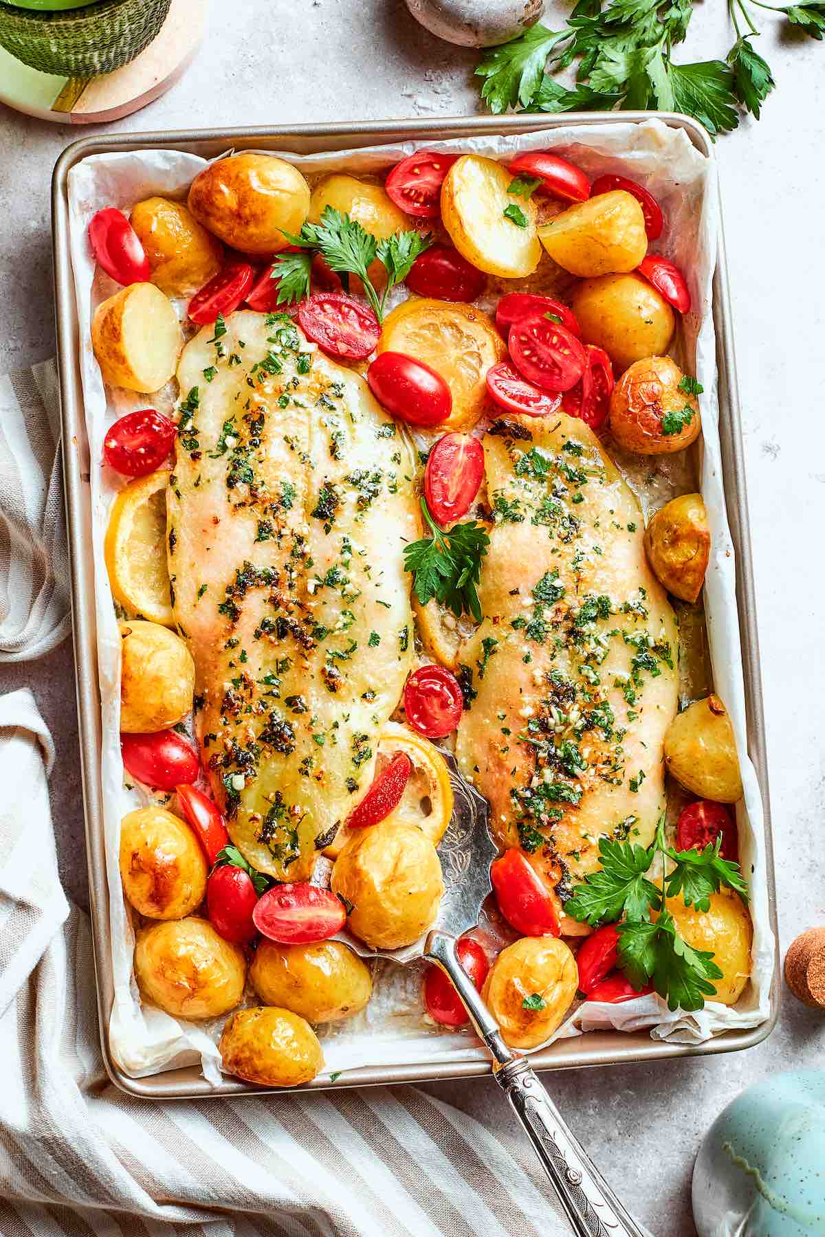 baked pollock on a baking sheet with roasted potatoes and halved cherry tomatoes.