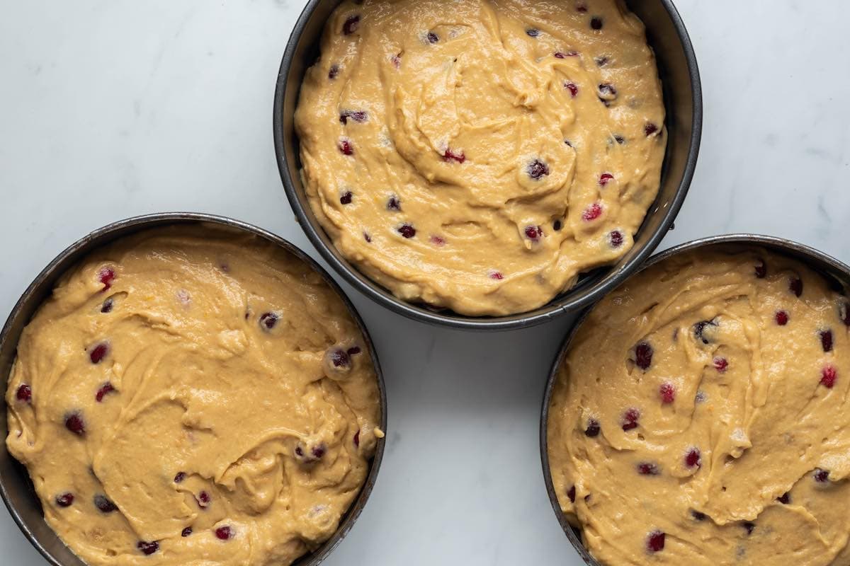 cranberry orange cake batter in three cake pans.
