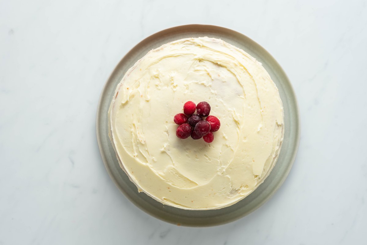 frosted cranberry orange cake on a plate with decorative cranberries on top.