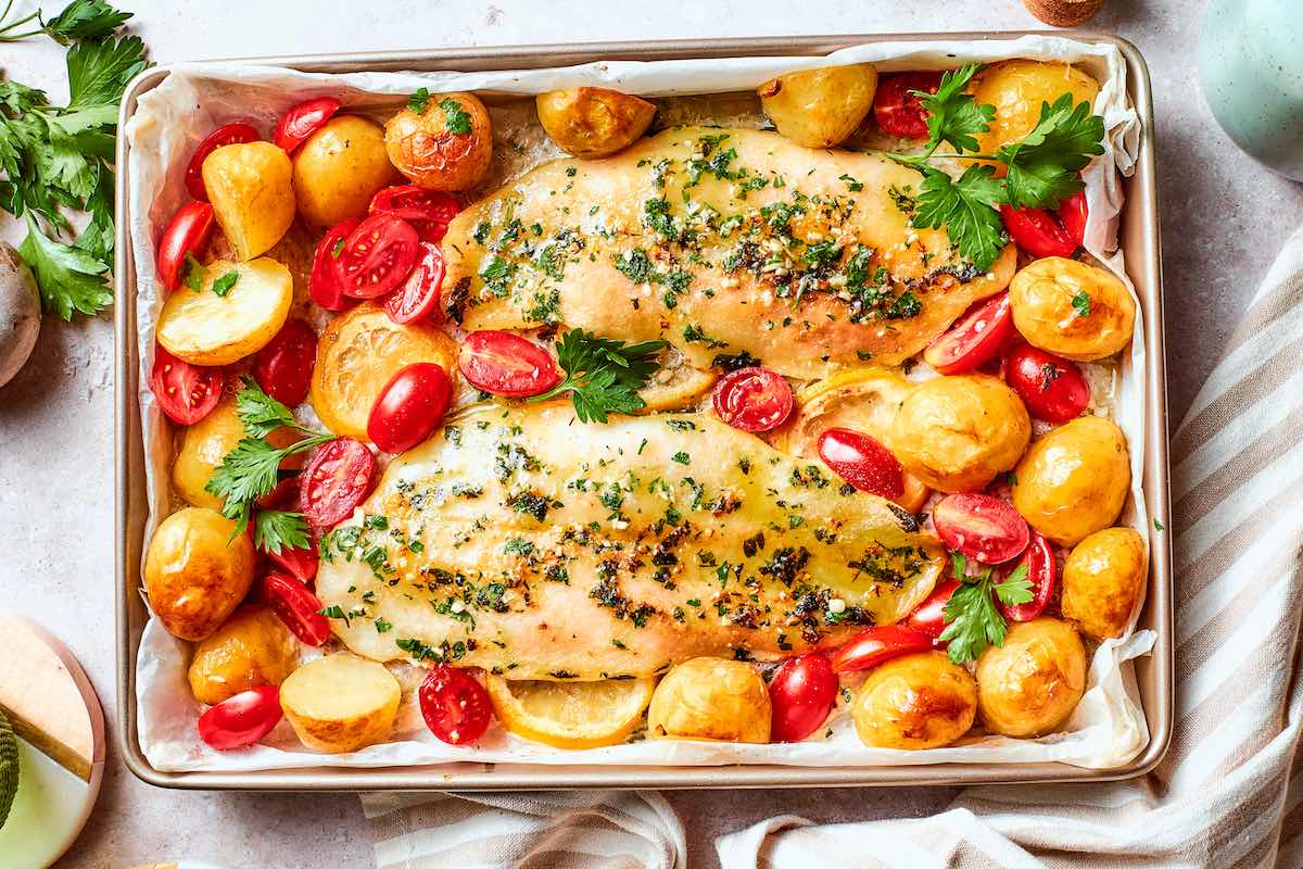 baked pollock on a baking dish with potatoes and cherry tomatoes.