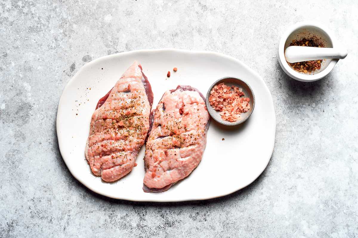 seasoned raw duck breasts on a plate.